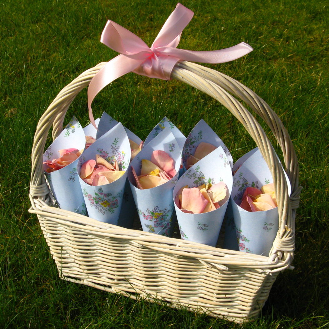 A Small White Bsket with a light pink ribbon handle holding Blue Flowers Patterned Confetti Cones filled with Blushing Pink Small Natural Rose Petal confetti