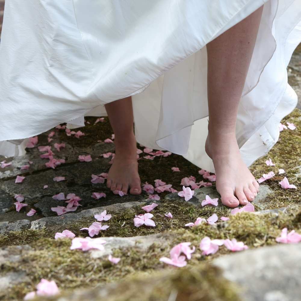 A barefoot bride walks up a flight of mossy flagstone steps that have been scattered with Hydrangea Petals.