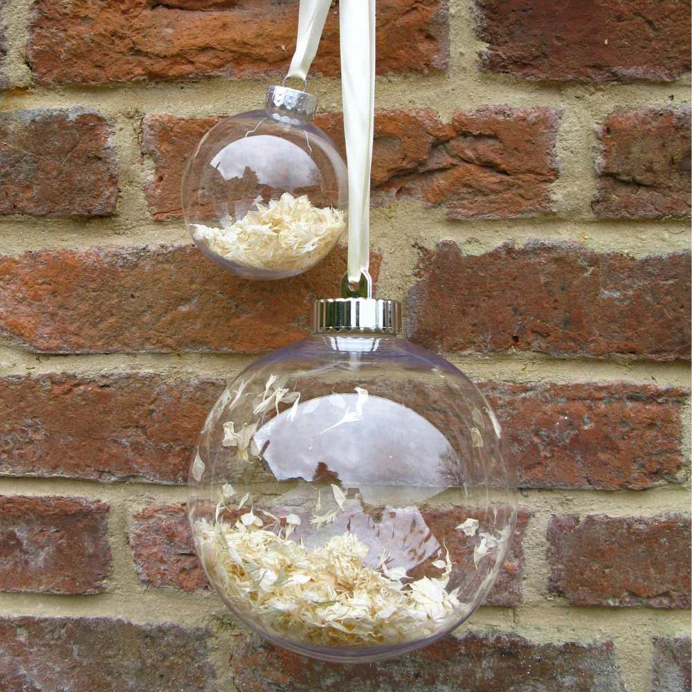 Large and Small white confetti filled Snow Baubles hanging against a brick wall.
