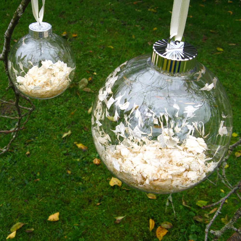 Large and Small white confetti filled Snow Baubles hanging from a tree branch.